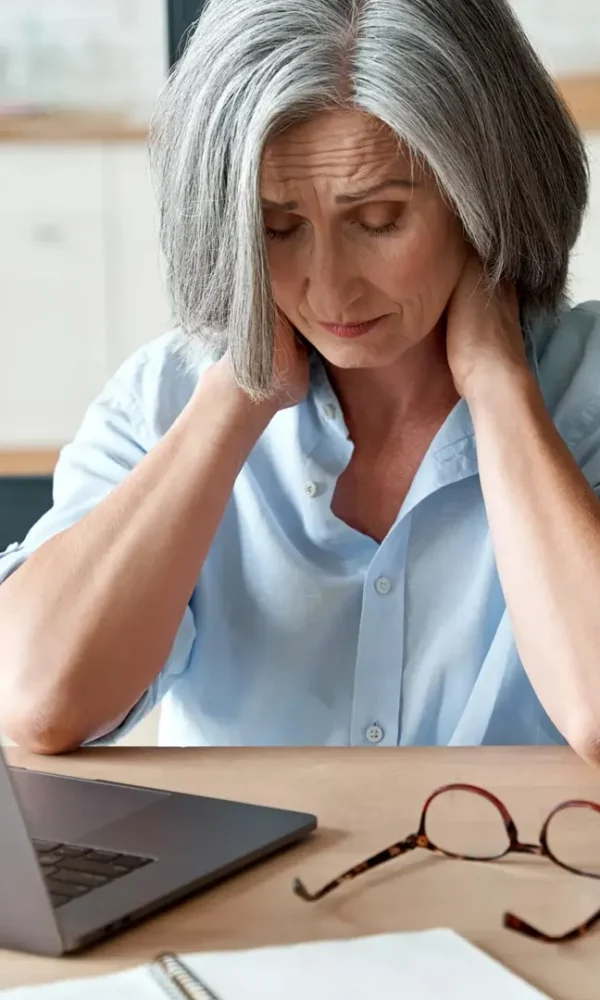 خانم مسن پر استرس پشت میز کار با لپتاپ و عینک و فنجان صورتی
